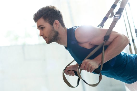 Mann stützt sich in den Schlingentrainer während einem TRX Training