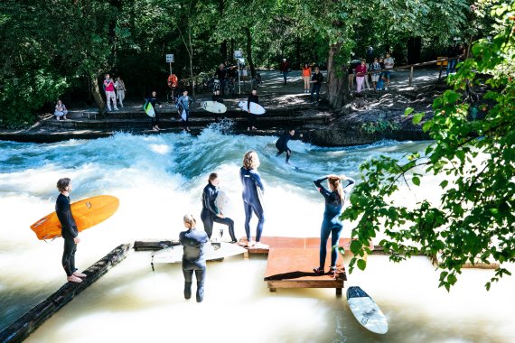 Surfer*innen am Fluss und auf dem Board im Wasser.