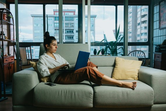 Frau liegt mit Laptop auf dem Sofa