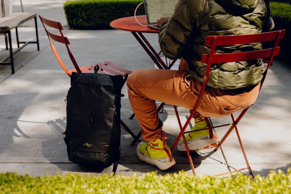 Person sitzt am Tisch, daneben ein Rucksack