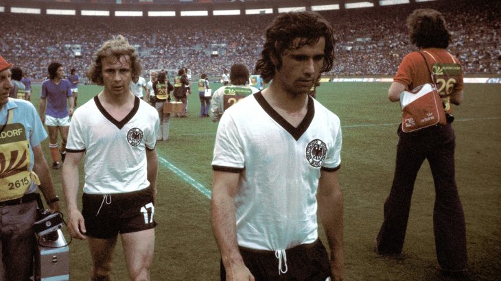 WM 1974: Ähnlich wie schon 1966 lief das DFB-Team in schlichten weißen Trikots mit V-Ausschnitt, schwarzem Kragen und schwarzen Ärmelenden auf. Im eigenen Land holten Gerd Müller (r.) und Co. in diesem Outfit den zweiten WM-Titel.