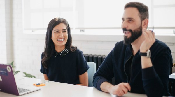 Eine Frau und ein Mann sitzen gut gelaunt an einem Bürotisch. 